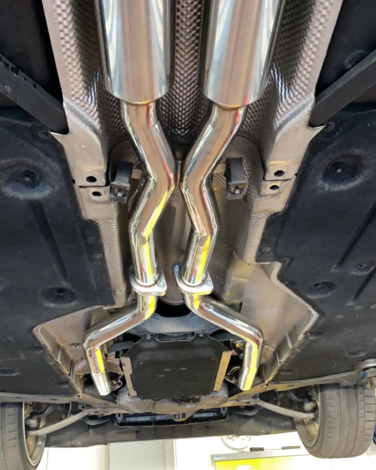 Système d'échappement inox avec X-Pipe sur une sportive, vue sous le pont élévateur